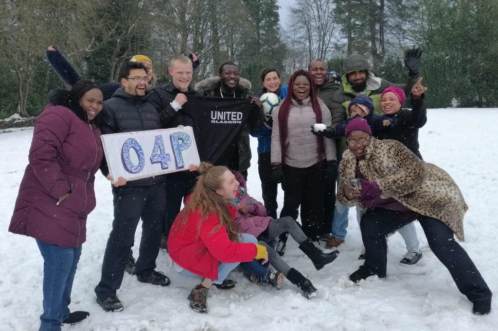 Group of people in the snow, two have fallen over and everyone is laughing.