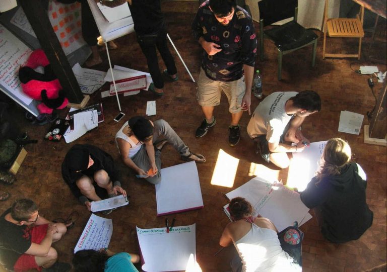 A group of people photographed from above. some are on the floor, one is standing and pointing
