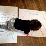 A baby with dark curly hair crawls across flipcharts with writing on them