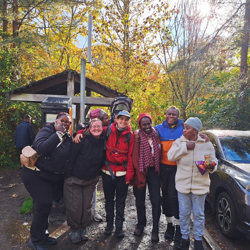 A group of people in boots an rain gear smiling at the camera, there are autumn leaves behind them and the sun is shining